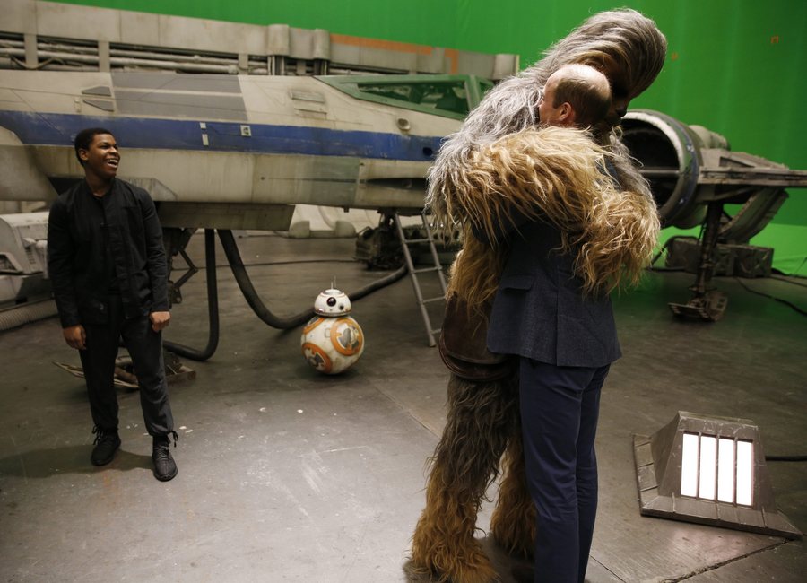 epa05267210 Britain's Prince William, Duke of Cambridge (R) is hugged by Chewbacca as British actor John Boyega smiles during a tour of the Star Wars sets at Pinewood studios in Iver Heath, west of London on April 19, 2016. Prince William and Prince Harry are touring Pinewood to visit the production workshops and meet the creative teams working behind the scenes on the Star Wars films. EPA/STR UK OUT
