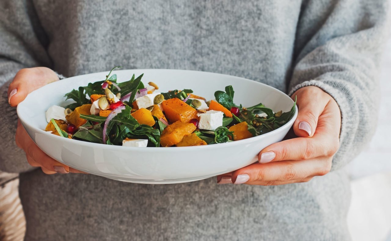 Woman Holding A Bowl Of Salad With Pumpkin, Arugula, Feta Cheese And Pomegranate Seeds.