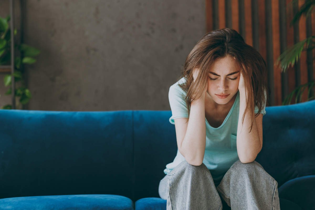 Young Frustrated Ill Woman She 20s Wear Casual Clothes Mint T Shirt Holding Head Suffer From Headache Close Eyes Sit On Blue Sofa Indoor Rest At Home In Own Room Apartment. People Lifestyle Concept