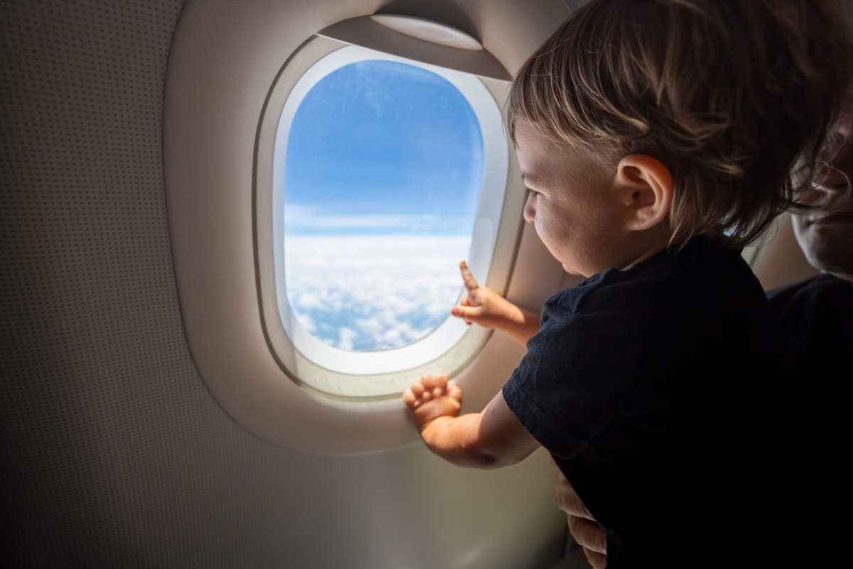 Cute Toddler Points His Finger At The Sky Through The Window. First Flight Concept, Traveling With Children.