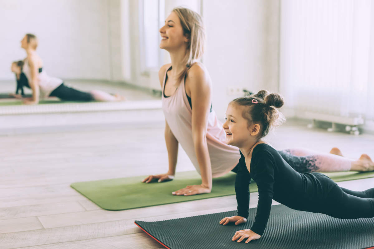 Sporty Woman And Child Girl Doing Stretching Exercise On Yoga Mat In Front Of Mirror In Fitness Class