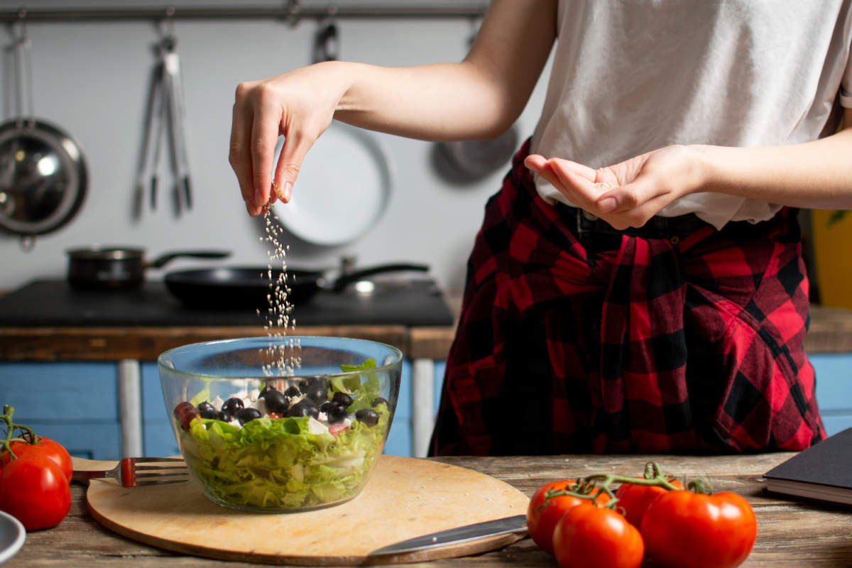 Young Girl Prepares A Vegetarian Salad In The Kitchen, She Salts And Adds Spices, The Process Of Preparing Healthy Food