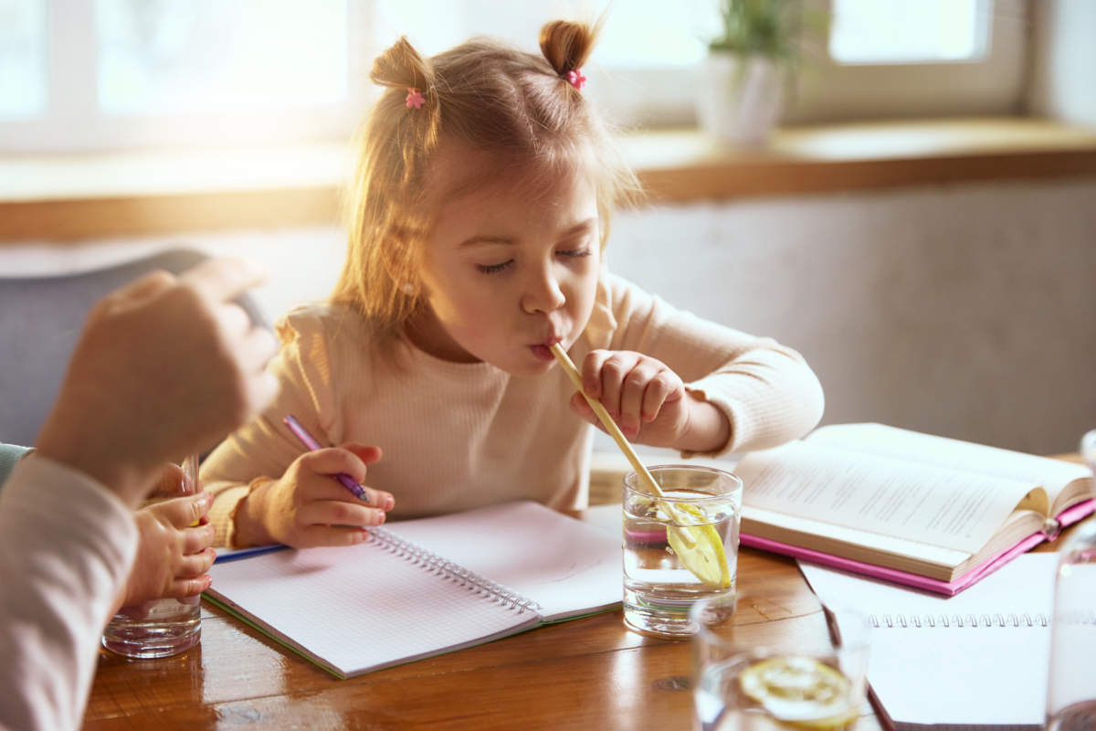 Little Girl Drinking Water With Lemon While Drawing At Table.