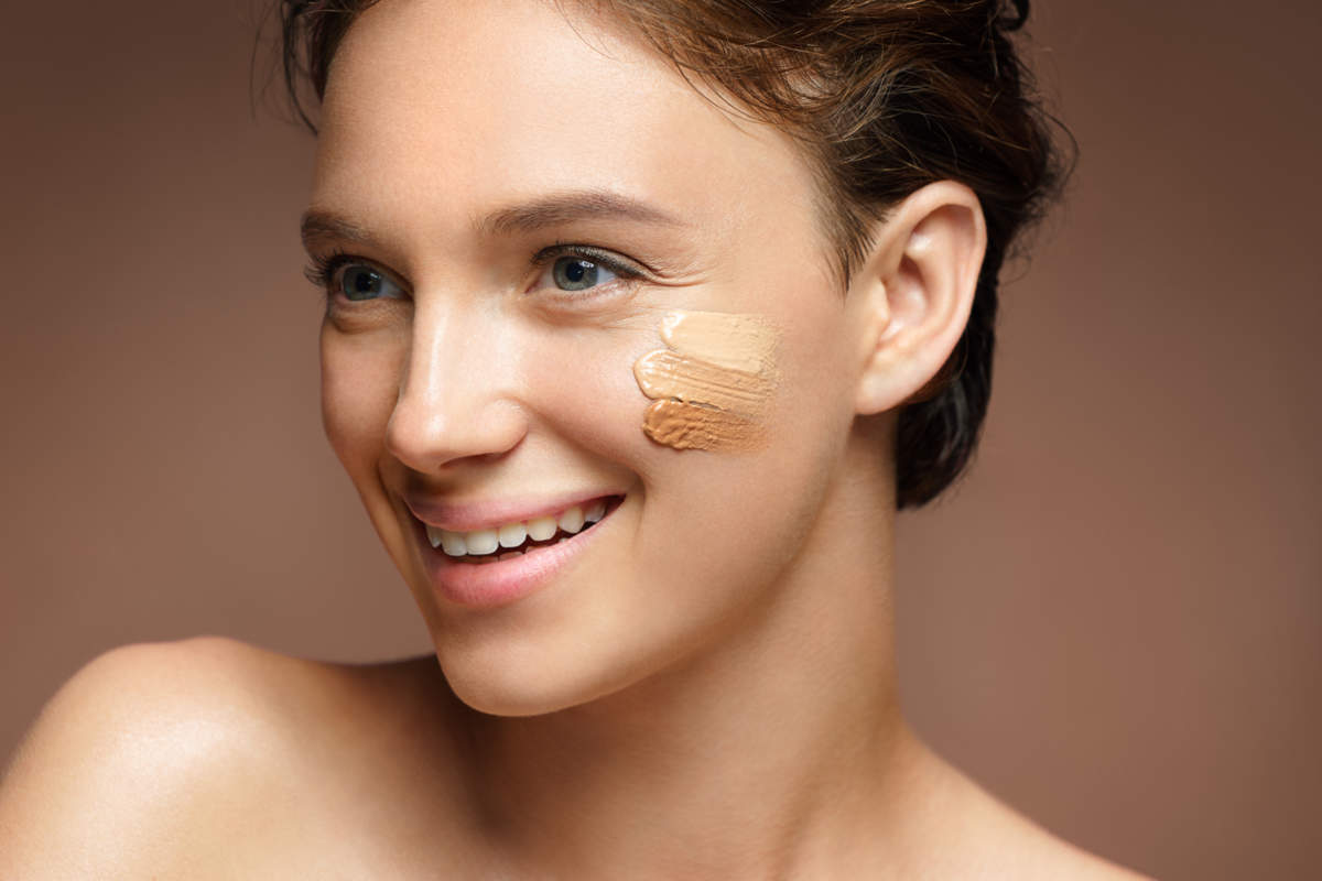 Beautiful Woman With Tone Cream Lines On Her Face. Photo Of Smiling Brunette Woman With Perfect Makeup On Brown Background. Skin Care Concept