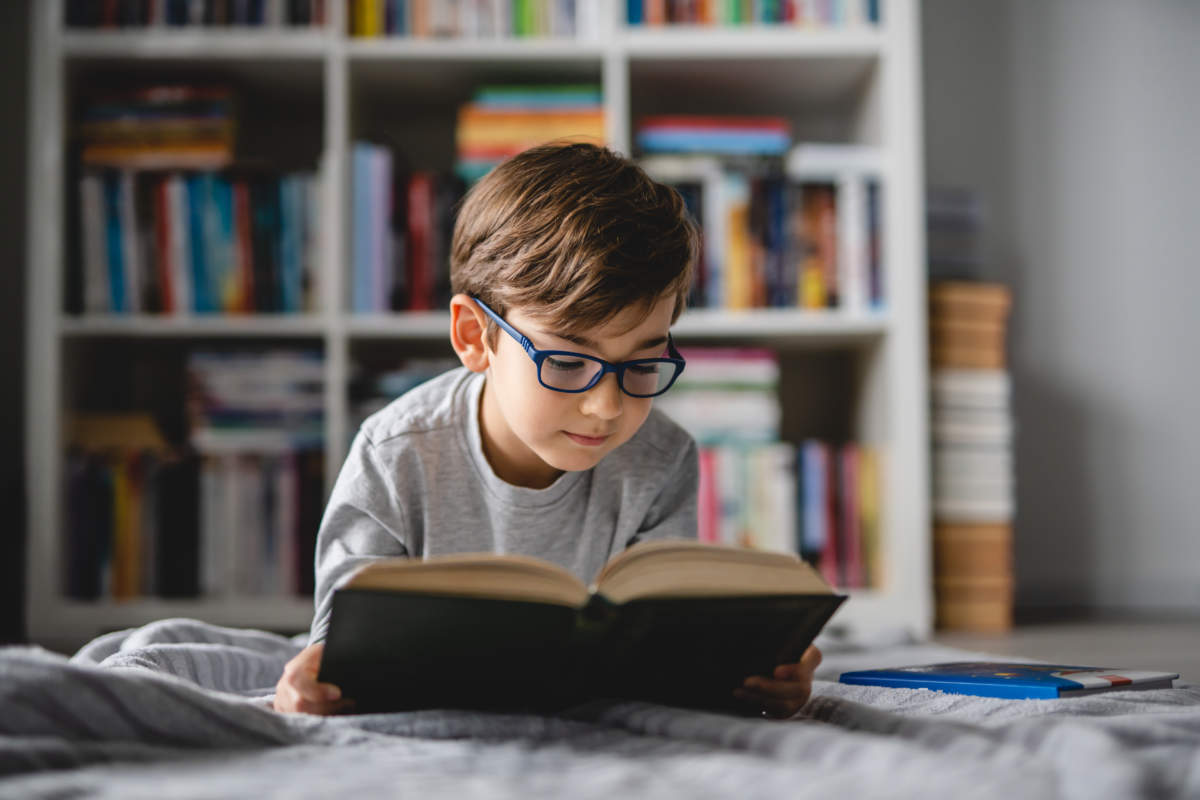 One Caucasian Boy Lying On The Floor At Home In Day Reading A Bo